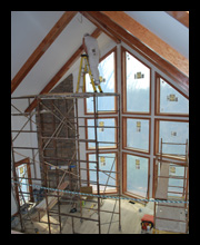 Contemporary new residence under construction in Albemarle County, Virginia, with loft overlooking great room with natural wood beams at vaulted ceiling, stone fireplace and large windows overlooking stream with mountain views beyond, designed by Candace Smith Architect